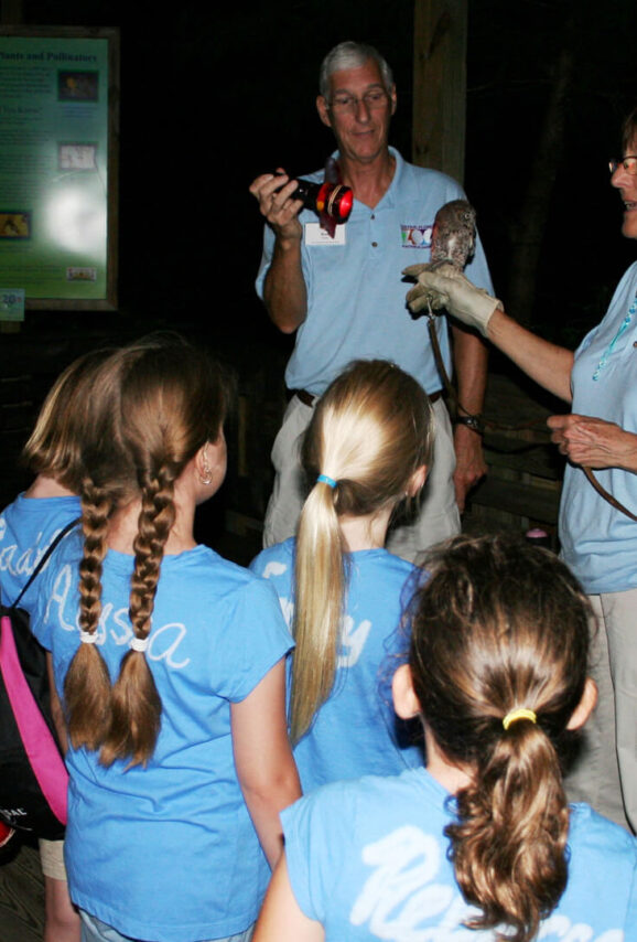 Children view an eastern screech owl by flashlight during Night Hike at the Zoo