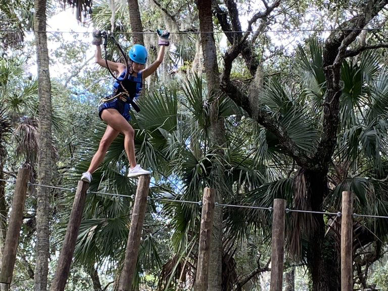 Young woman enjoying Seminole Aerial Adventures walking above trees at the Central Florida Zoo